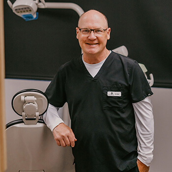 Dr. Robert Swenson smiling and leaning on a dental chair